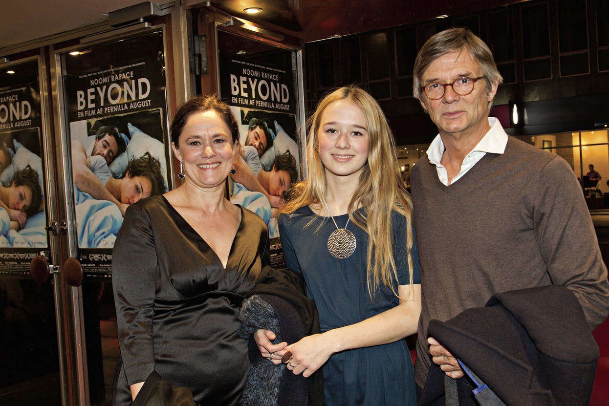 Alba August with parents Bille August and Pernilla August posing standing inside a movie theatre